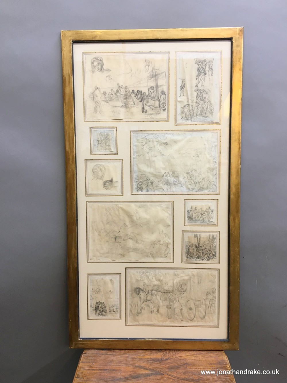 A large gilded wooden frame displaying a collection of eleven individual 18th-century graphite sketches mounted on an off-white mat.