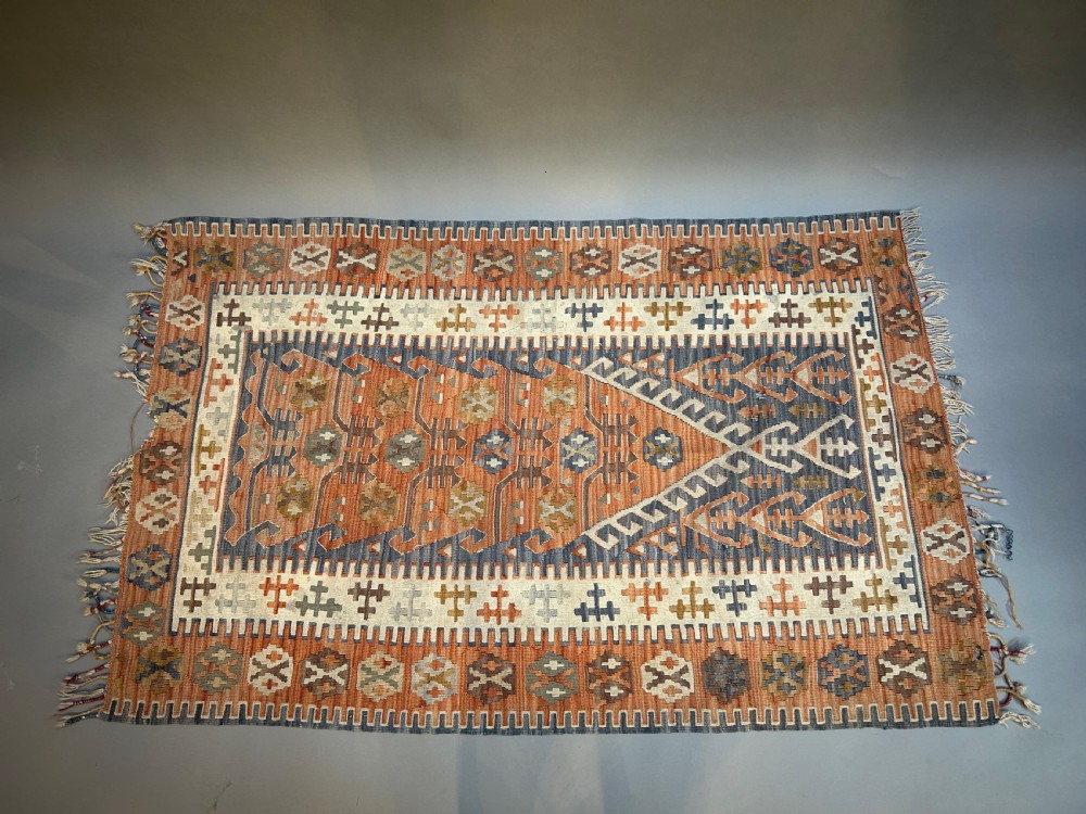 A vintage handwoven Turkish kilim rug featuring geometric tribal patterns in terracotta, indigo blue, and cream with fringed edges.
