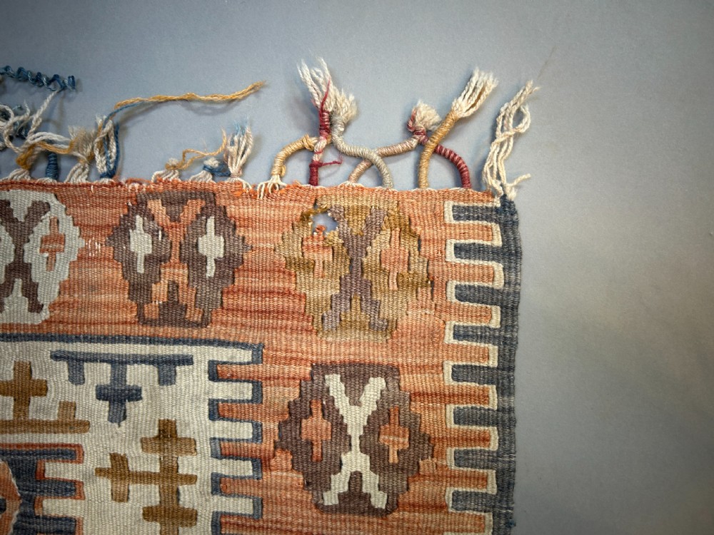 A vintage handwoven Turkish kilim rug featuring geometric tribal patterns in terracotta, indigo blue, and cream with fringed edges. View II