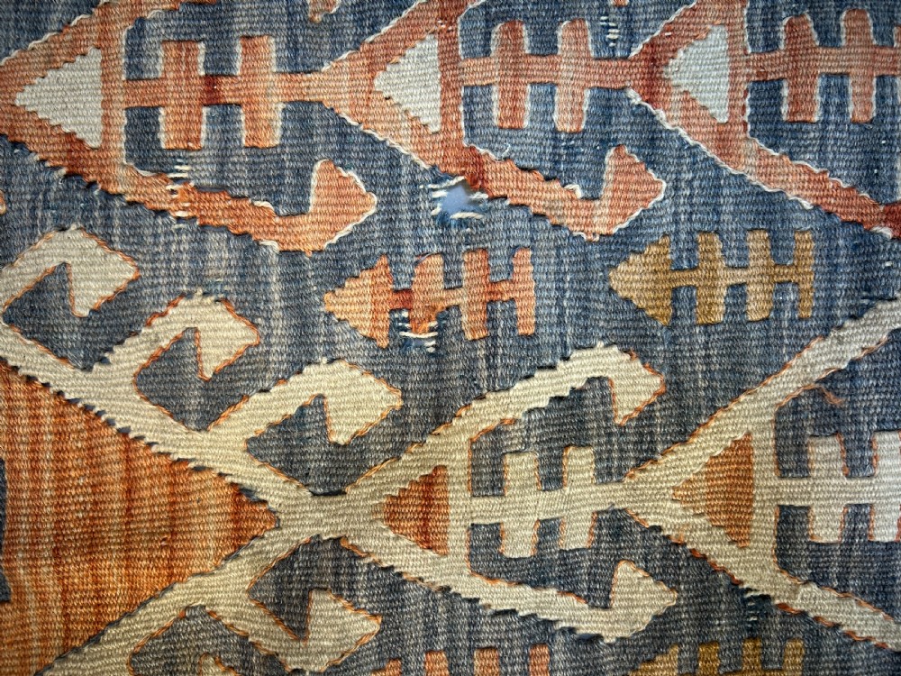 A vintage handwoven Turkish kilim rug featuring geometric tribal patterns in terracotta, indigo blue, and cream with fringed edges. View III