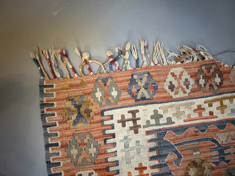 A vintage handwoven Turkish kilim rug featuring geometric tribal patterns in terracotta, indigo blue, and cream with fringed edges. View V