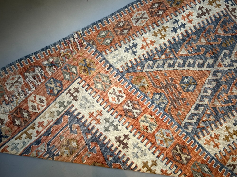 A vintage handwoven Turkish kilim rug featuring geometric tribal patterns in terracotta, indigo blue, and cream with fringed edges. View VI