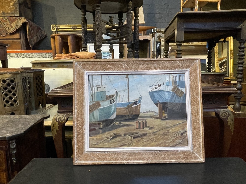 An oil painting on board depicting fishing boats drydocked in a boatyard, framed in light limed wood. View VI