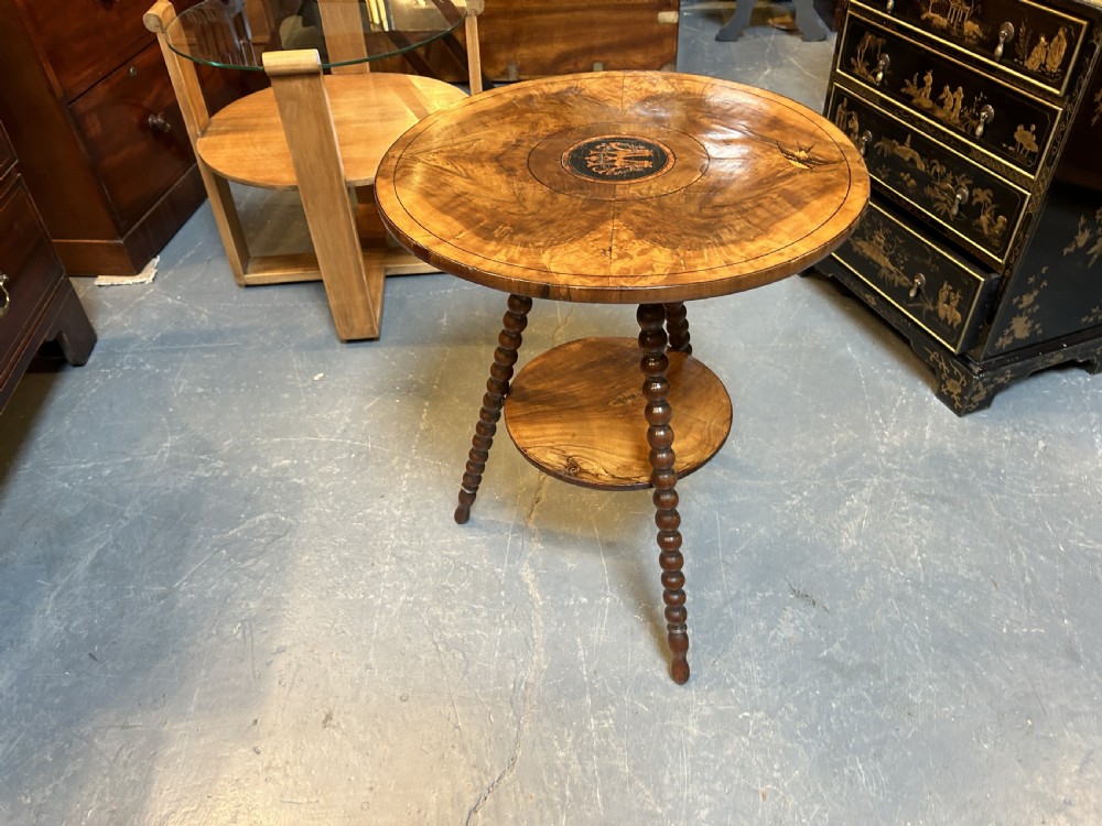A 19th-century Italian circular occasional table made of warm brown burr walnut with a central marquetry motif, three bobbin-turned legs, and a lower tier shelf. View II