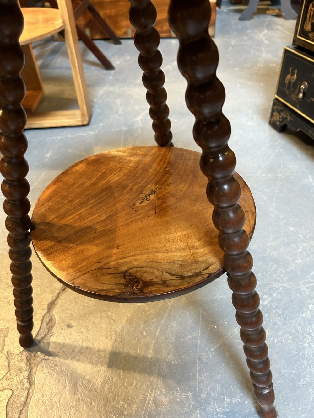 A 19th-century Italian circular occasional table made of warm brown burr walnut with a central marquetry motif, three bobbin-turned legs, and a lower tier shelf. View V