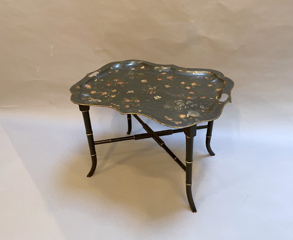 A Victorian black painted toleware tray table with hand-painted floral motifs, a scalloped edge, and faux bamboo legs.