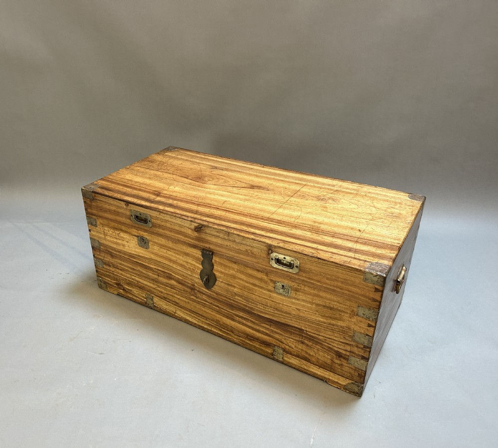 An antique rectangular camphor wood campaign trunk with flush metal handles, corner brackets, exposed dovetail joinery, and a central latch.