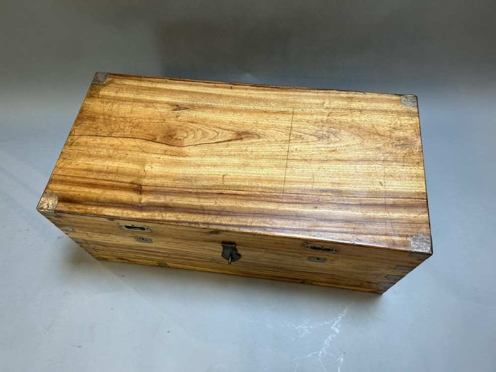 An antique rectangular camphor wood campaign trunk with flush metal handles, corner brackets, exposed dovetail joinery, and a central latch. View II