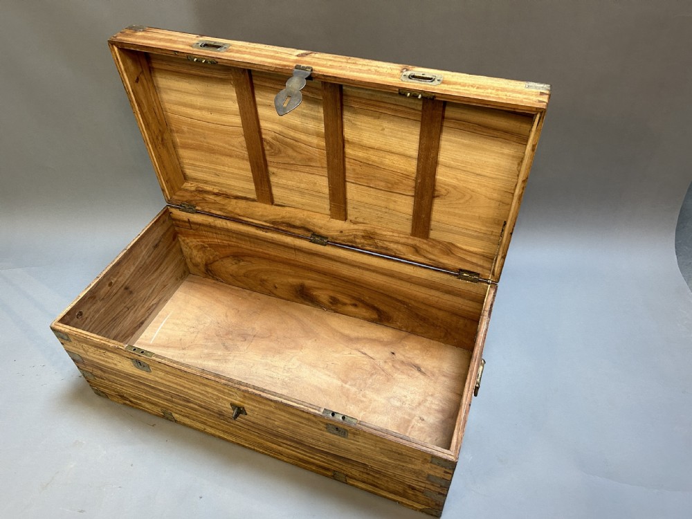 An antique rectangular camphor wood campaign trunk with flush metal handles, corner brackets, exposed dovetail joinery, and a central latch. View IV