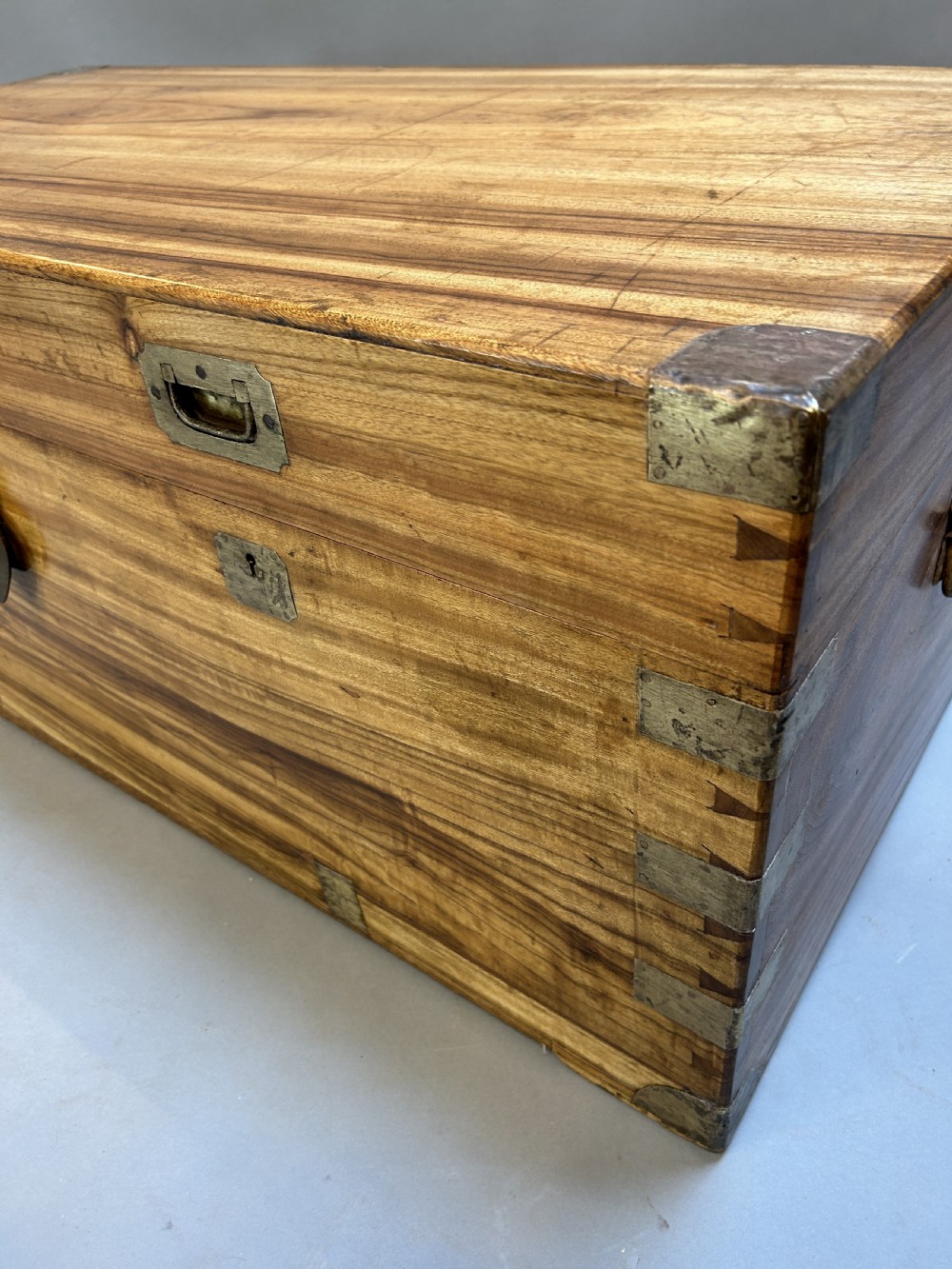 An antique rectangular camphor wood campaign trunk with flush metal handles, corner brackets, exposed dovetail joinery, and a central latch. View V