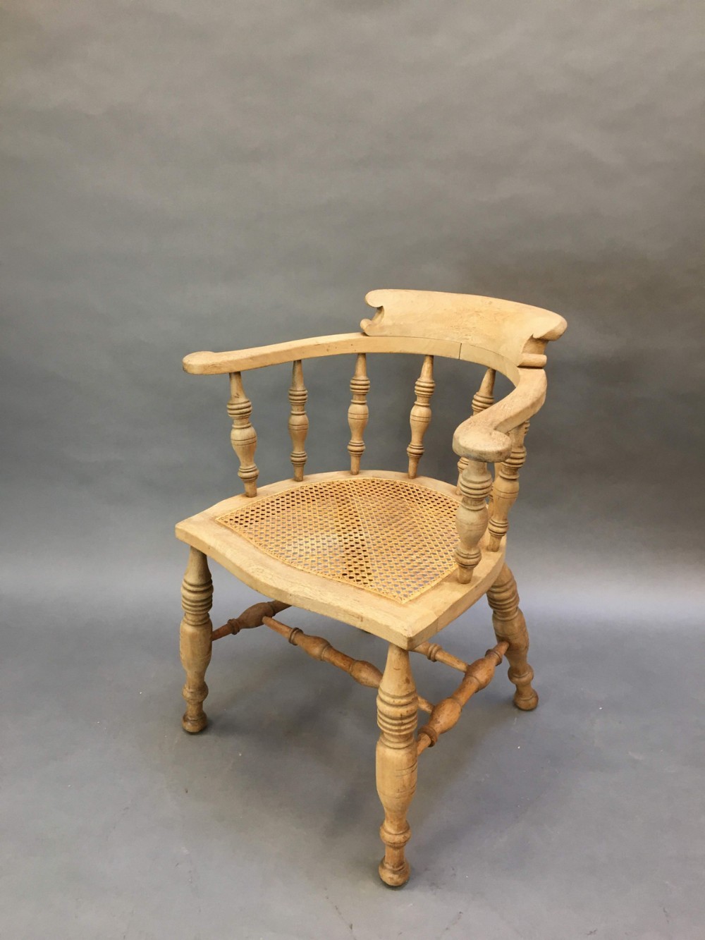 A nineteenth-century mahogany captains armchair featuring turned spindles, a low curved backrest, and a woven cane seat.