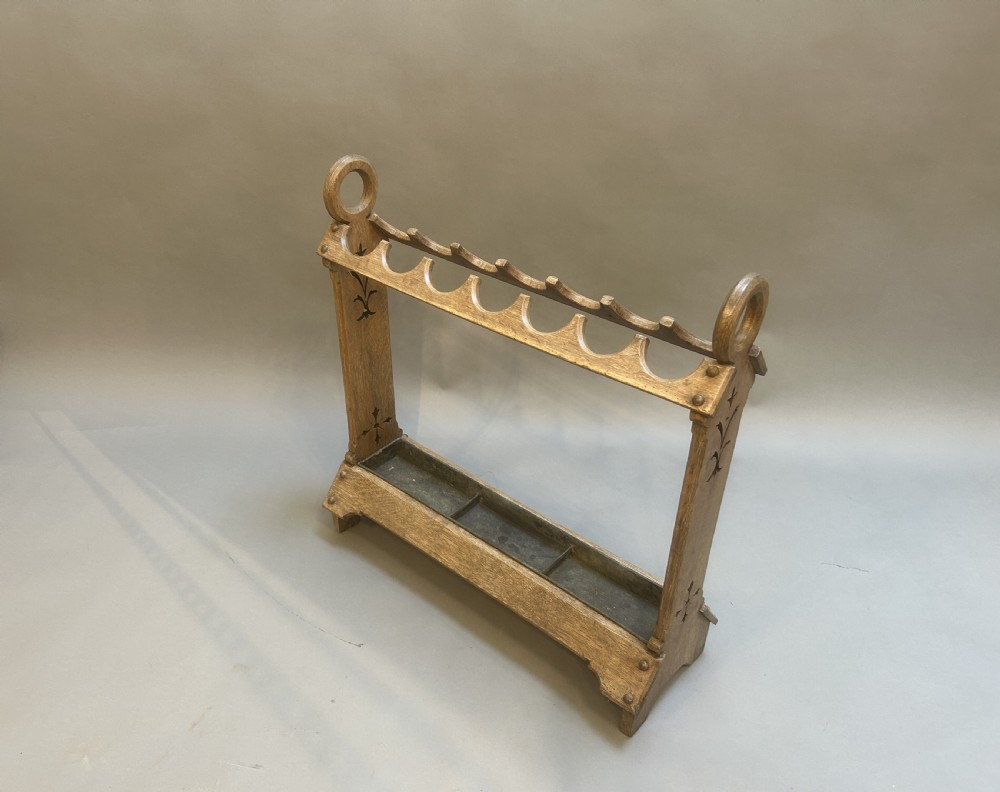 An antique oak umbrella and stick stand featuring a scalloped upper rail, carved ring handles, inlaid side uprights, and a metal drip tray at the base.