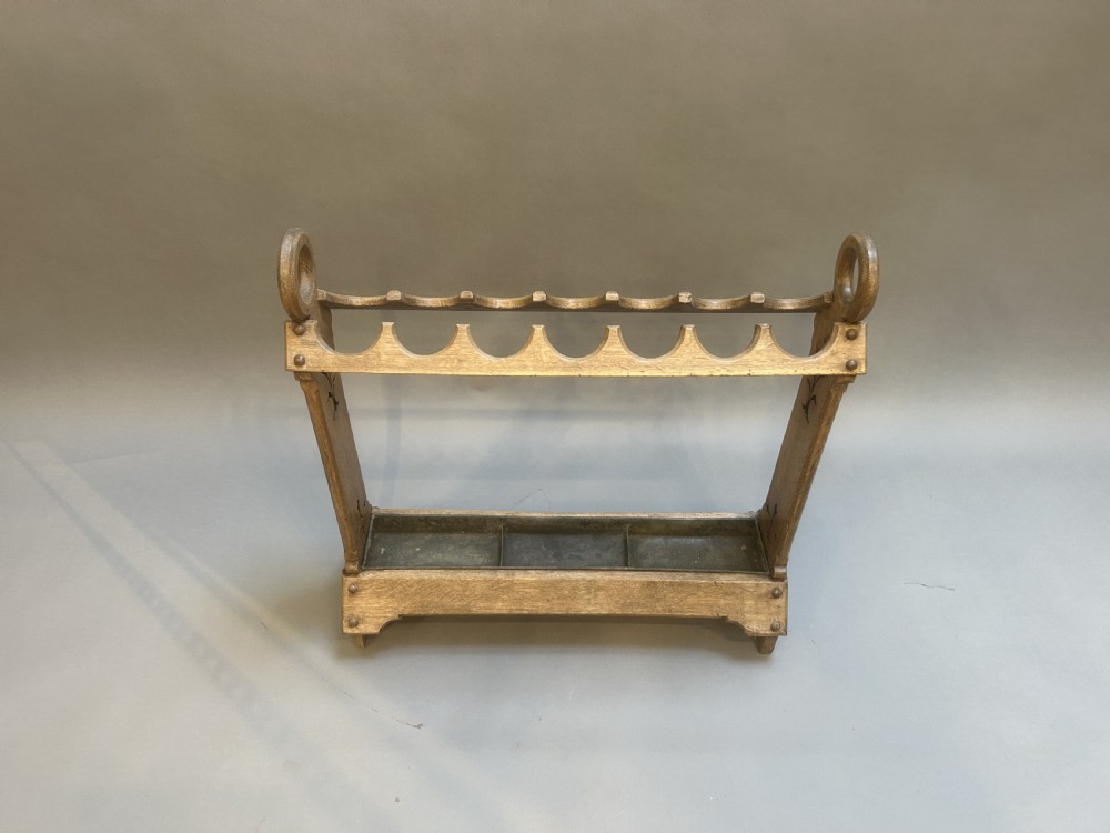 An antique oak umbrella and stick stand featuring a scalloped upper rail, carved ring handles, inlaid side uprights, and a metal drip tray at the base. View V