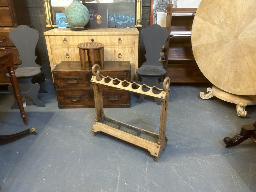 An antique oak umbrella and stick stand featuring a scalloped upper rail, carved ring handles, inlaid side uprights, and a metal drip tray at the base. View IX