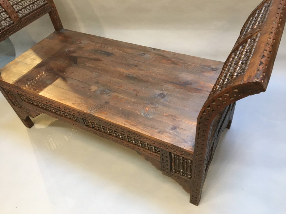 A dark brown carved wooden window seat featuring raised curved arms and geometric mashrabiya lattice panels along the base. View II