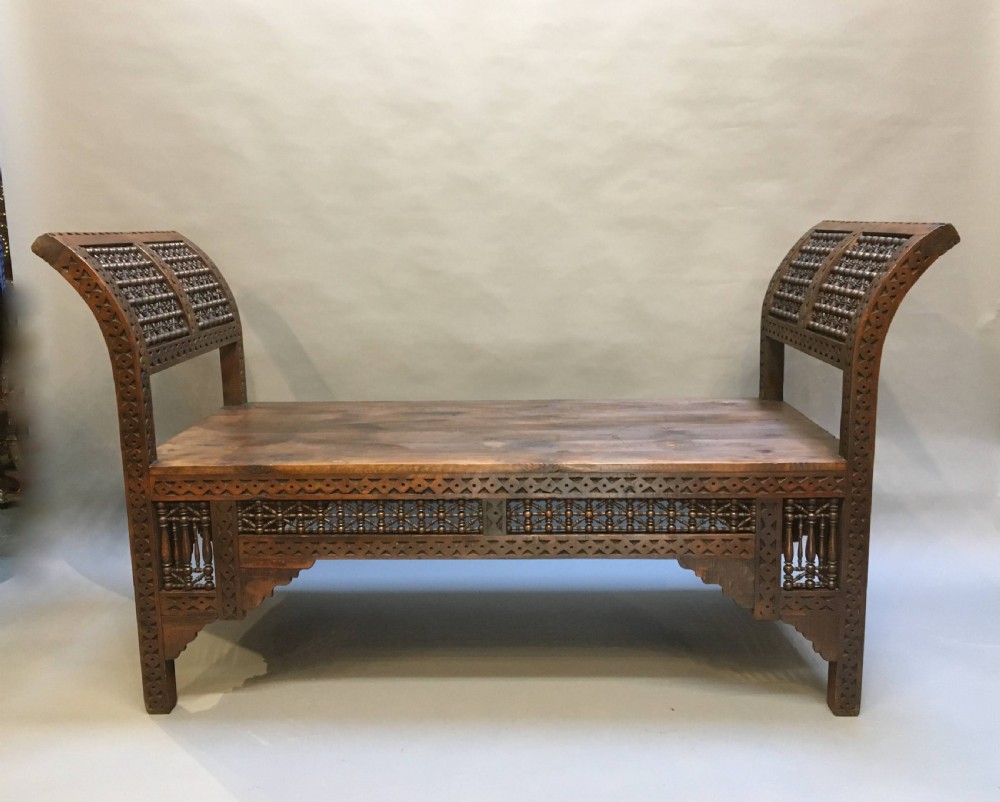 A dark brown carved wooden window seat featuring raised curved arms and geometric mashrabiya lattice panels along the base. View III