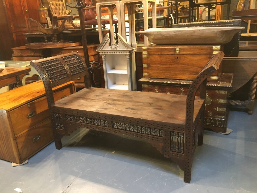 A dark brown carved wooden window seat featuring raised curved arms and geometric mashrabiya lattice panels along the base. View VIII