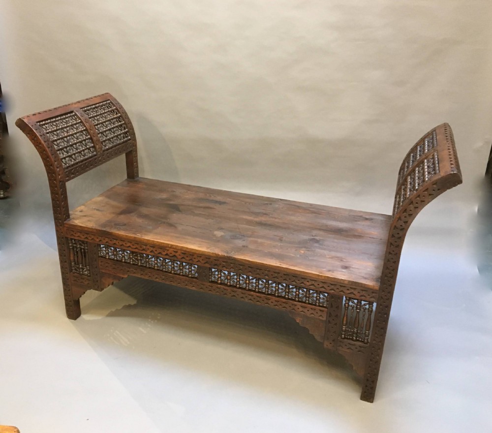 A dark brown carved wooden window seat featuring raised curved arms and geometric mashrabiya lattice panels along the base. View IX
