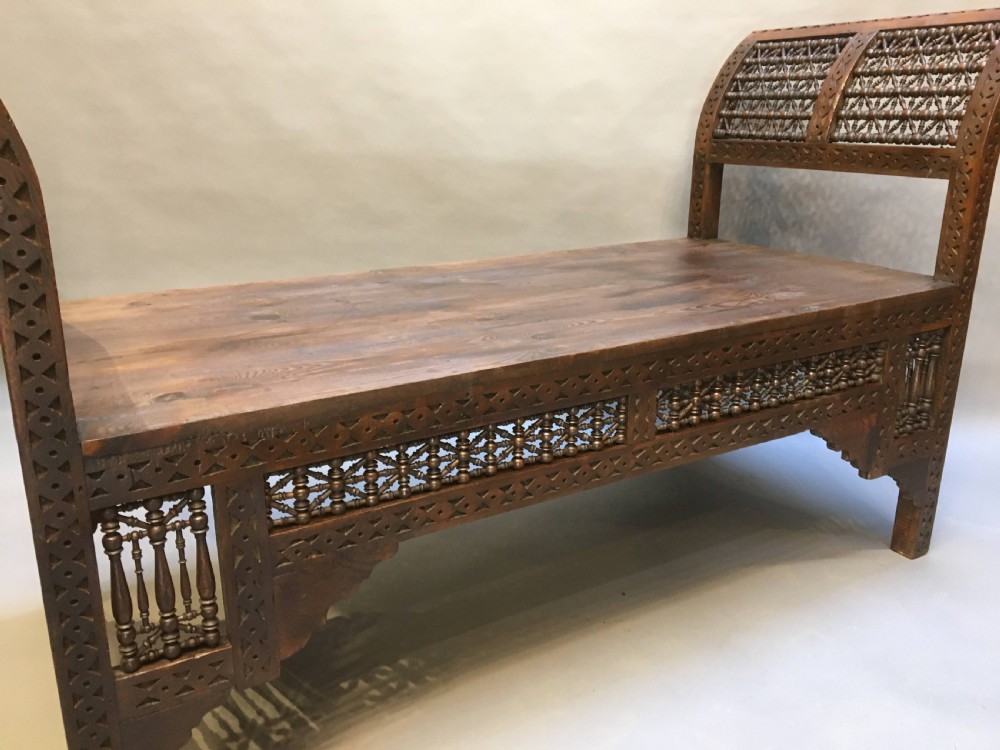 A dark brown carved wooden window seat featuring raised curved arms and geometric mashrabiya lattice panels along the base. View XI
