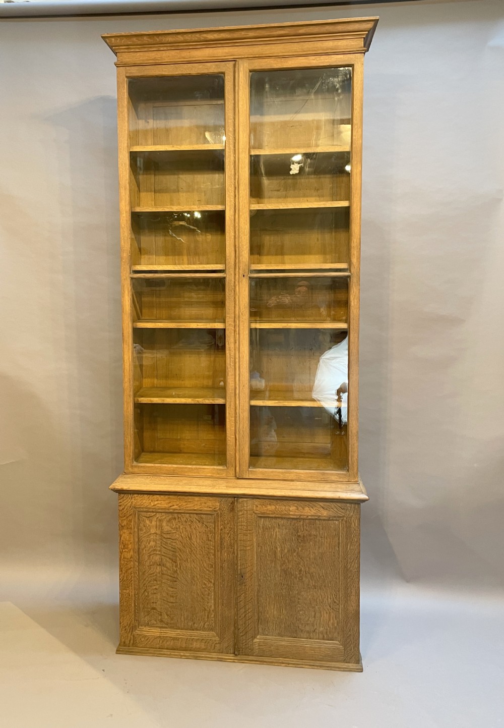 A tall Victorian light oak two-part bookcase with two upper glazed doors revealing adjustable shelves and a two-door cupboard base. View IV