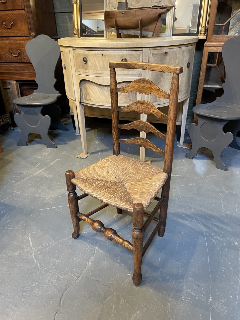 A wooden country side chair featuring a ladderback with four wavy horizontal slats, turned front legs, and a woven rush seat. View VII