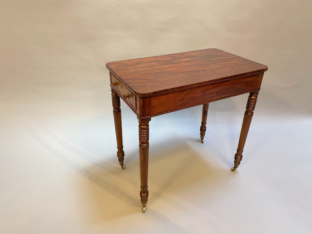A rectangular George IV mahogany occasional lamp table featuring a side drawer with wooden knobs, turned reeded legs, and brass castors.