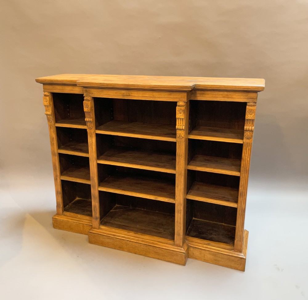 A Victorian low oak breakfront bookcase featuring open adjustable shelving, fluted pilasters with carved rosette motifs, and a solid plinth base.
