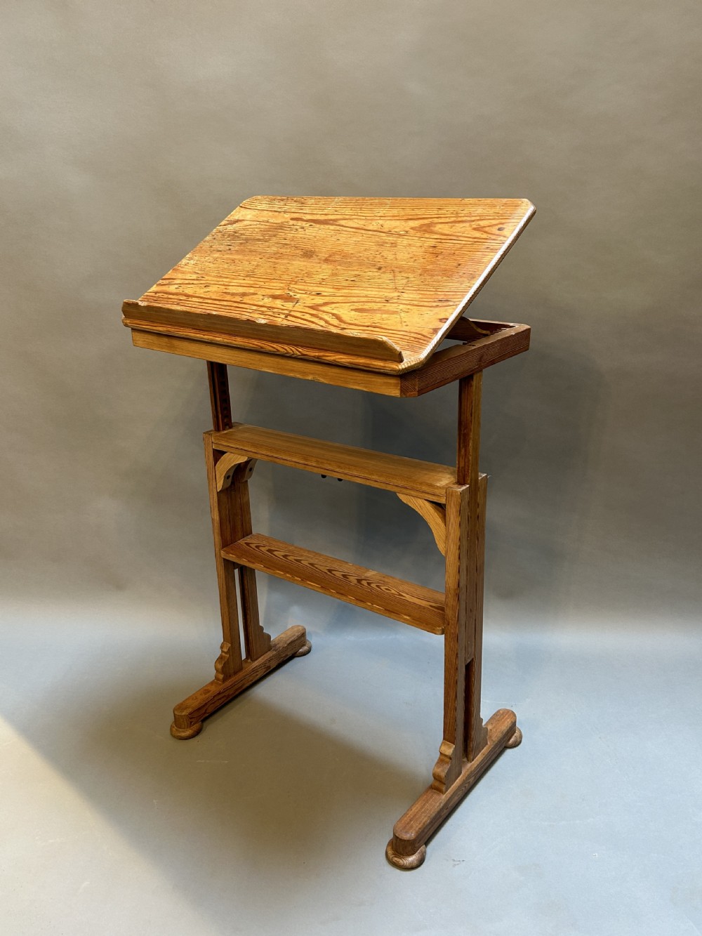 An early twentieth-century pine lectern table featuring a slanted reading surface with a retaining lip, supported by a trestle base with a lower shelf. View II