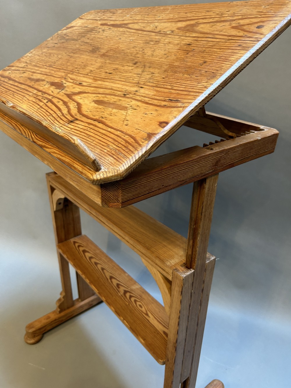 An early twentieth-century pine lectern table featuring a slanted reading surface with a retaining lip, supported by a trestle base with a lower shelf. View III