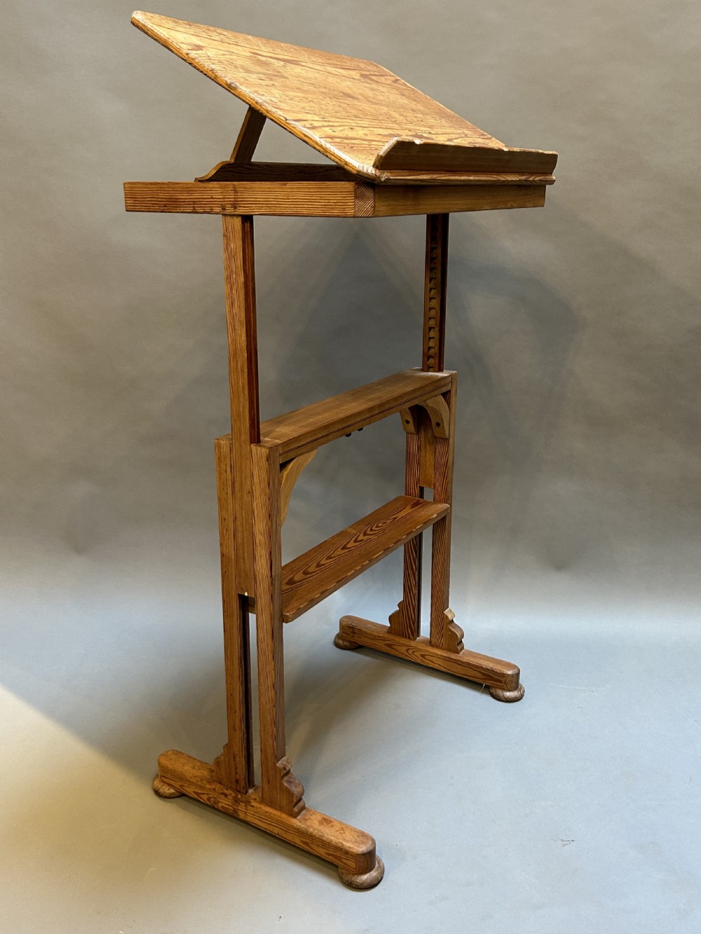 An early twentieth-century pine lectern table featuring a slanted reading surface with a retaining lip, supported by a trestle base with a lower shelf. View IV