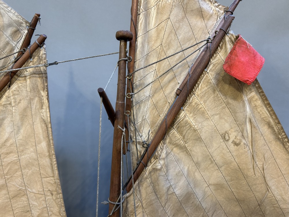 A large vintage wooden pond yacht with a two-masted schooner rig, aged sails, and a white and brown painted hull mounted on a dark wooden stand. View VI
