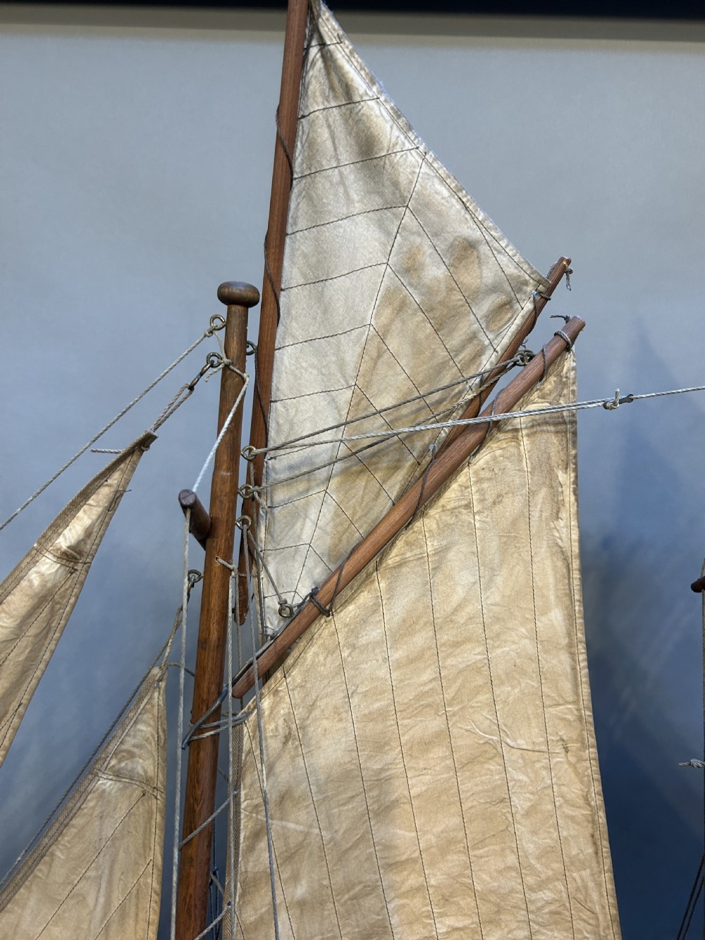 A large vintage wooden pond yacht with a two-masted schooner rig, aged sails, and a white and brown painted hull mounted on a dark wooden stand. View VII