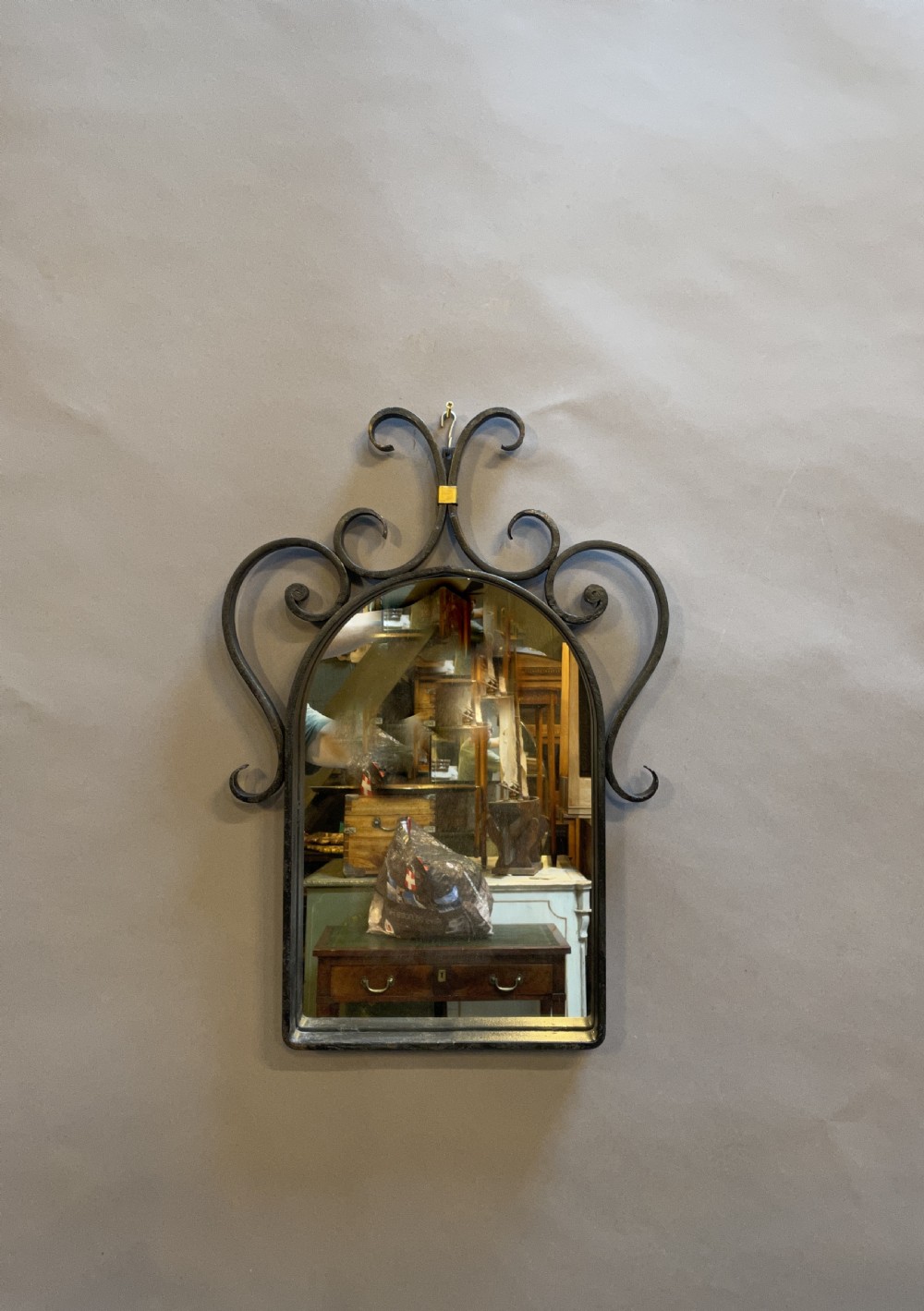 An arched wall mirror featuring a dark wrought iron frame with ornate top scrollwork and a small brass accent collar.