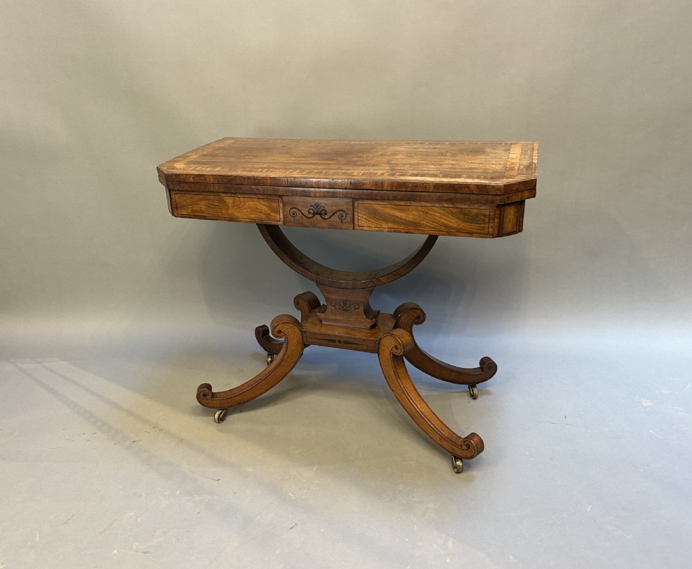 A Regency mahogany card table featuring a rectangular fold-over top with inlaid crossbanding, supported by a curved pedestal and splayed quadripod legs on brass castors.