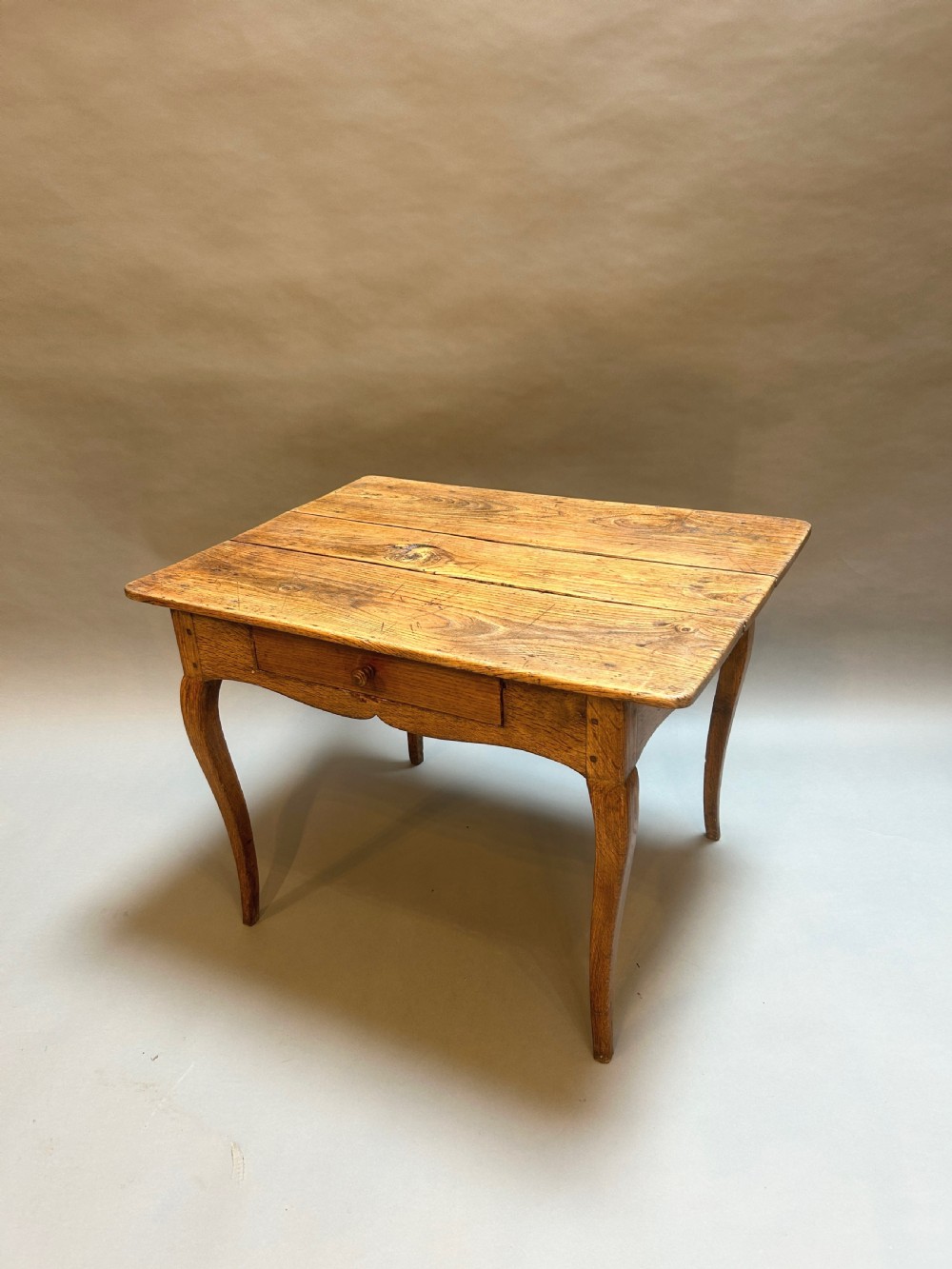 A French provincial wooden side table featuring slender cabriole legs, a single frieze drawer with a wooden knob, and a planked top.
