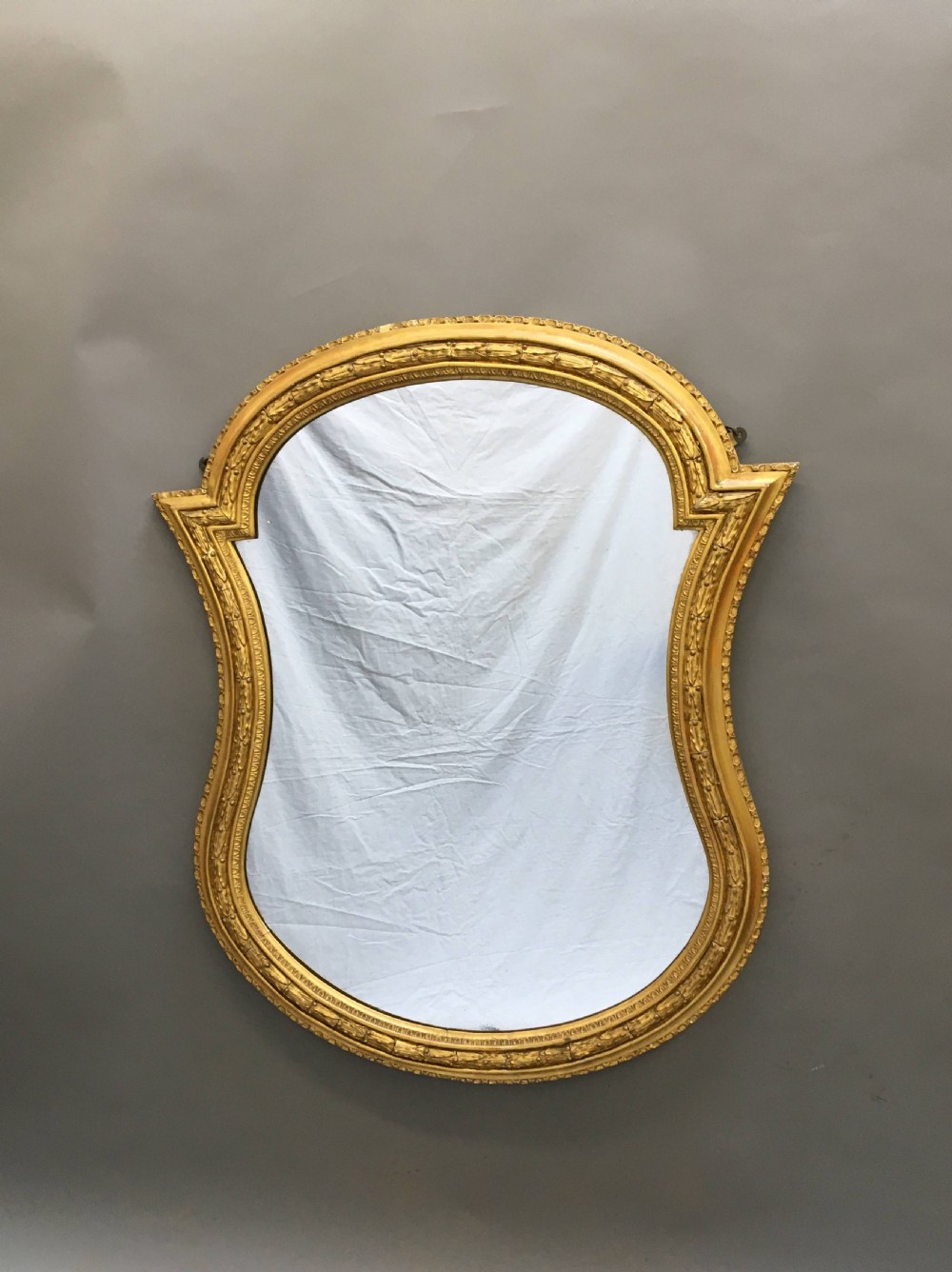 A large nineteenth-century shaped wall mirror featuring a gilded wooden frame with beaded moulding.