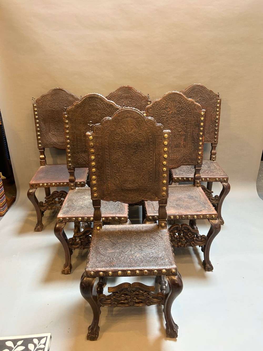 A set of six dark carved wooden dining chairs featuring embossed brown leather seats and backrests trimmed with brass studs.