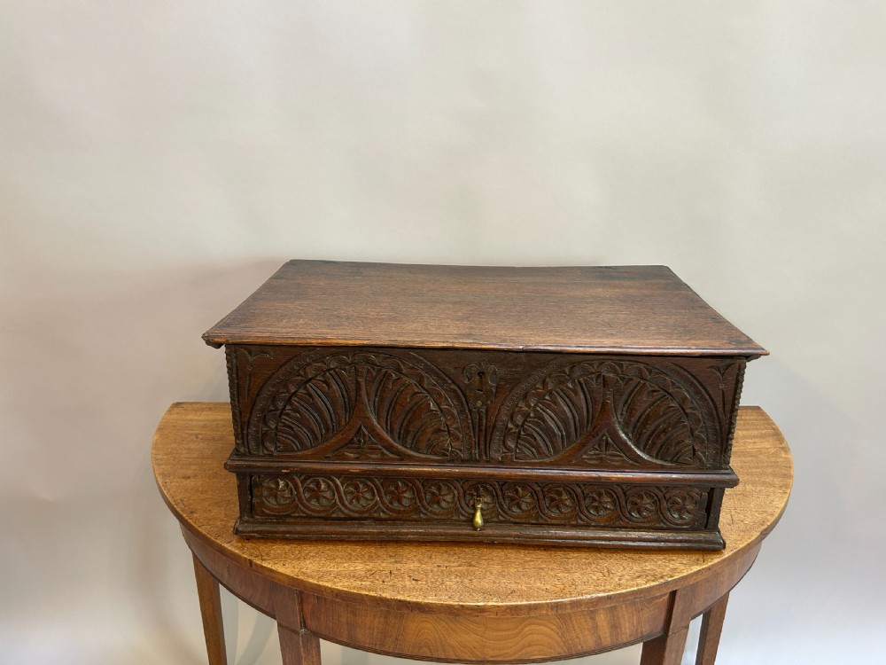 An eighteenth-century dark oak bible box featuring relief carved lunettes, a brass teardrop drawer pull, and a hinged lid.