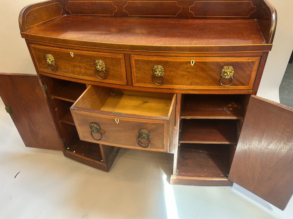 A George IV mahogany sideboard featuring a gallery back, geometric wood inlay, brass lion-mask handles, and pedestal cupboards flanking a central drawer. View IV