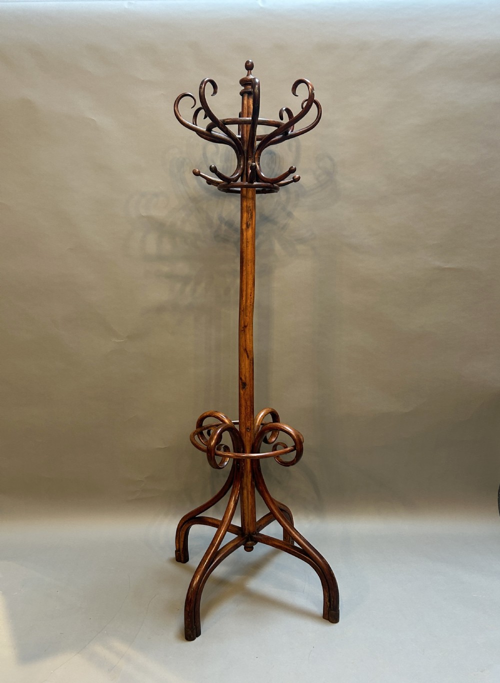 A tall dark brown bentwood hat and coat stand featuring multiple curved upper hooks, a central turned pole, and an integrated lower umbrella ring supported by four splayed legs.