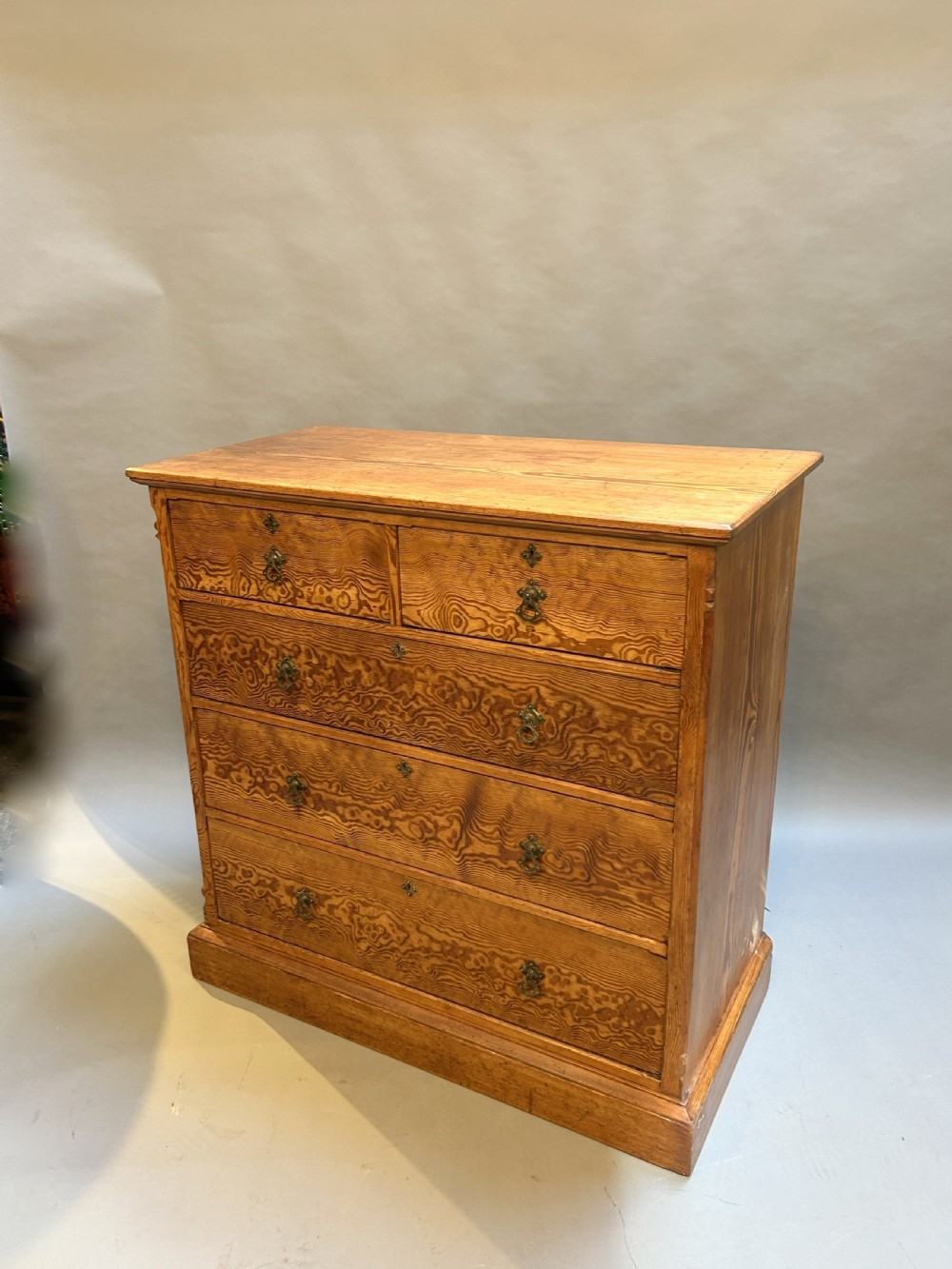 A Victorian Oregon pine chest of drawers featuring five drawers with prominent wavy wood grain and metal drop handles on a plinth base.