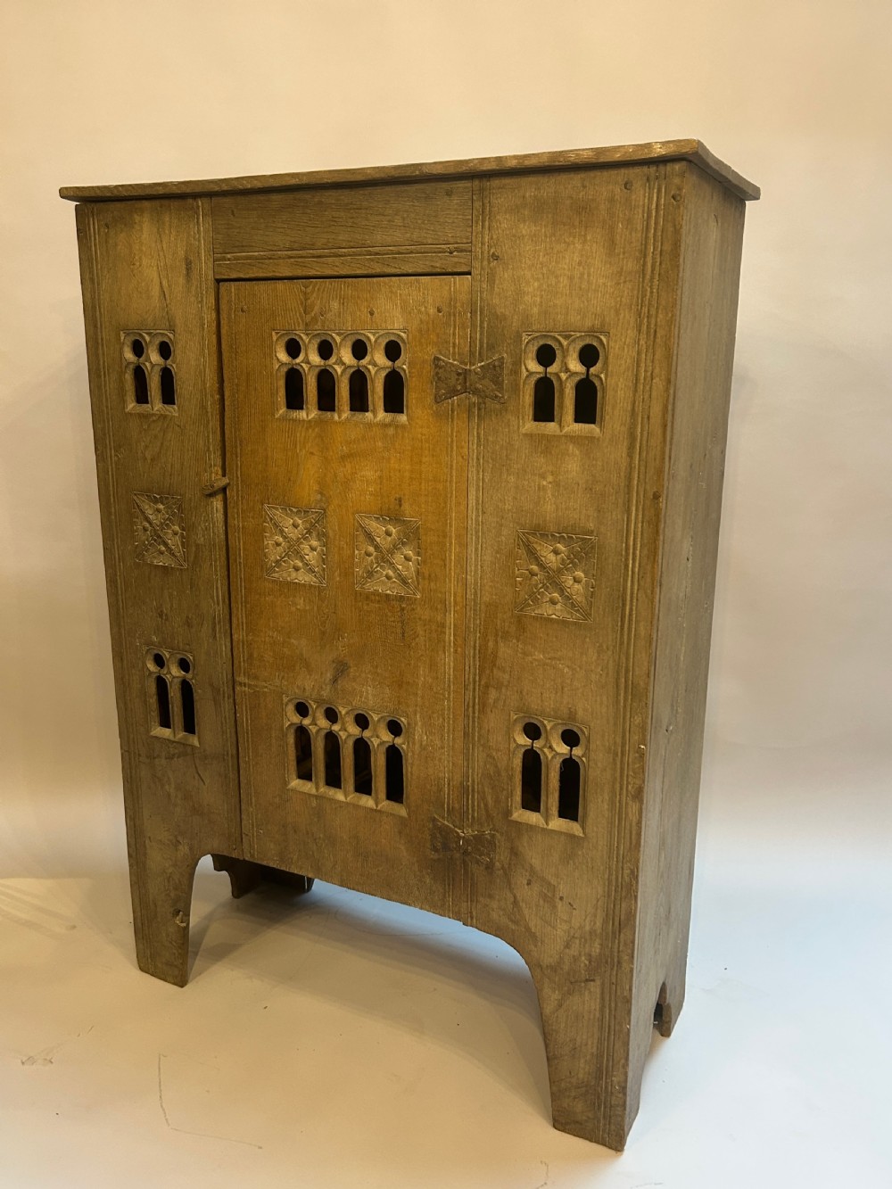 A tall natural wood Indian cupboard with hand-carved floral tiles, arched cutouts, and iron hinges.
