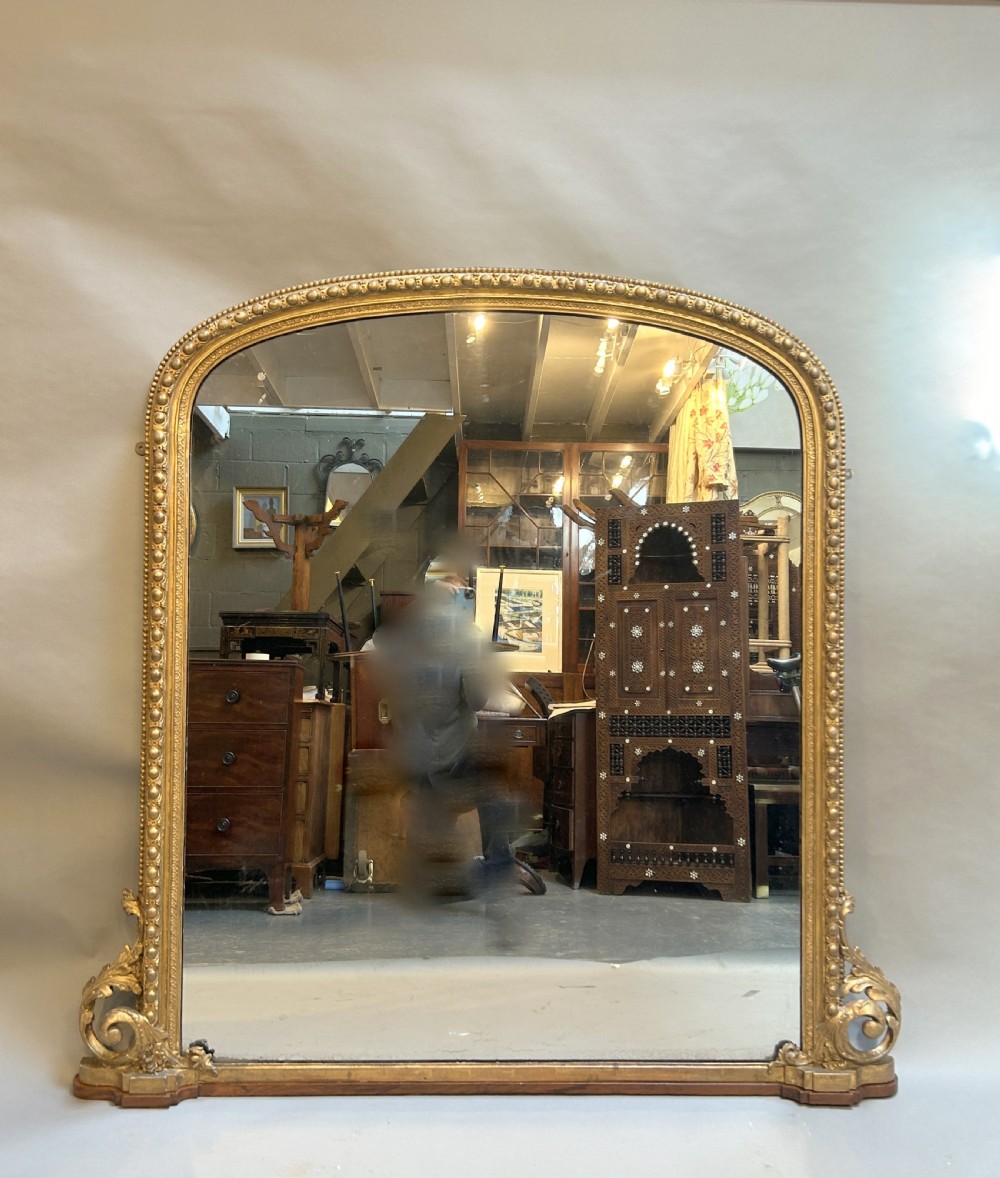 An arched Victorian giltwood overmantel mirror featuring beaded edging along the frame and carved acanthus leaf brackets at the base.