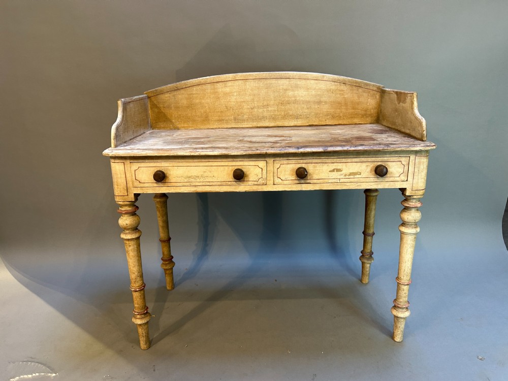 A Victorian cream painted writing table featuring a curved gallery backboard, two drawers with wooden turned knobs, and turned legs. View VII