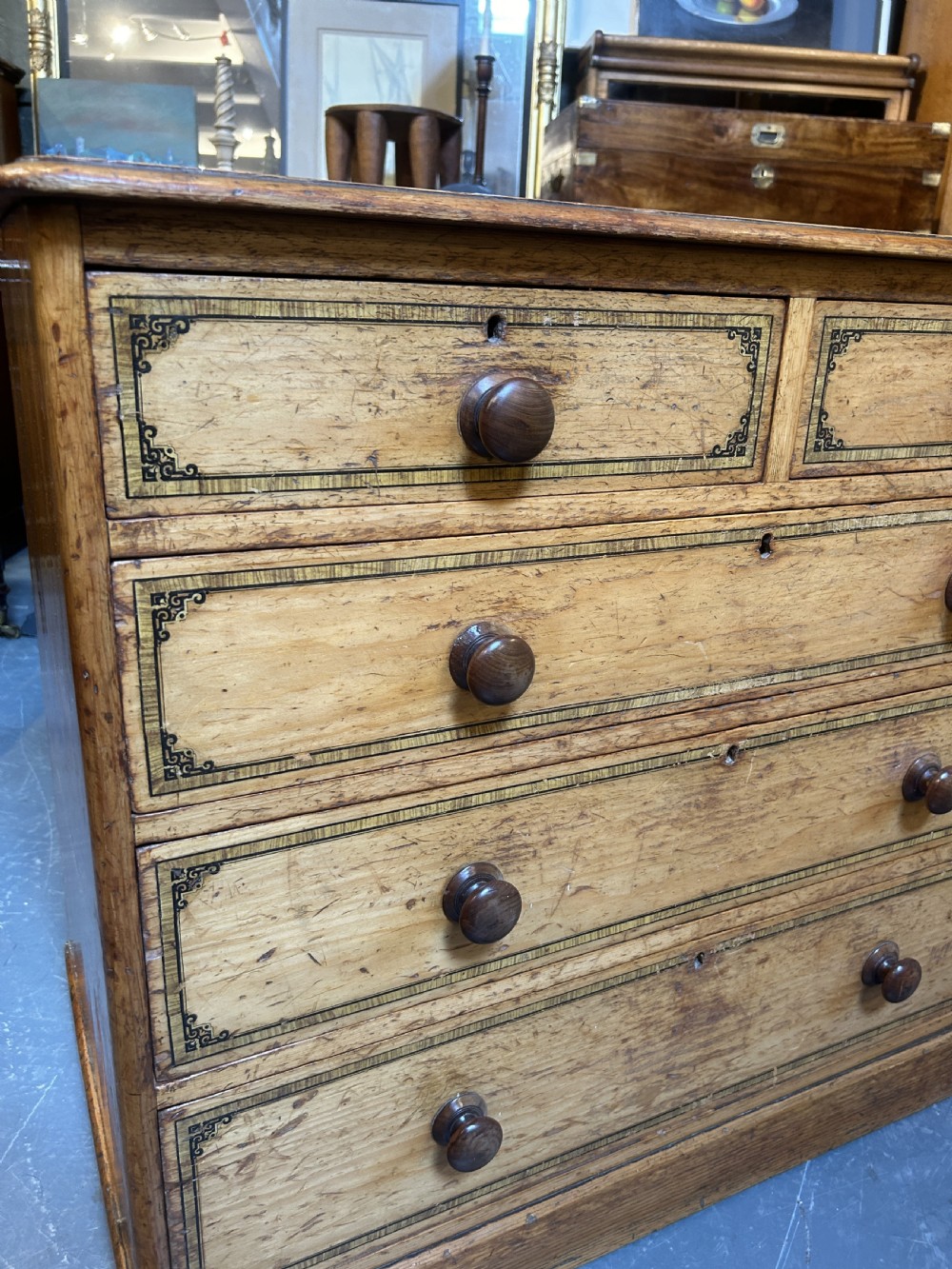 A Victorian pine chest of drawers with black stencilled borders, featuring two short drawers over three long drawers with turned wooden knobs. View IX