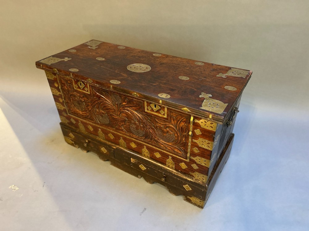 A 19th-century dark hardwood Zanzibar chest featuring relief floral carving, pierced brass plates, brass corner mounts, and three small lower drawers.