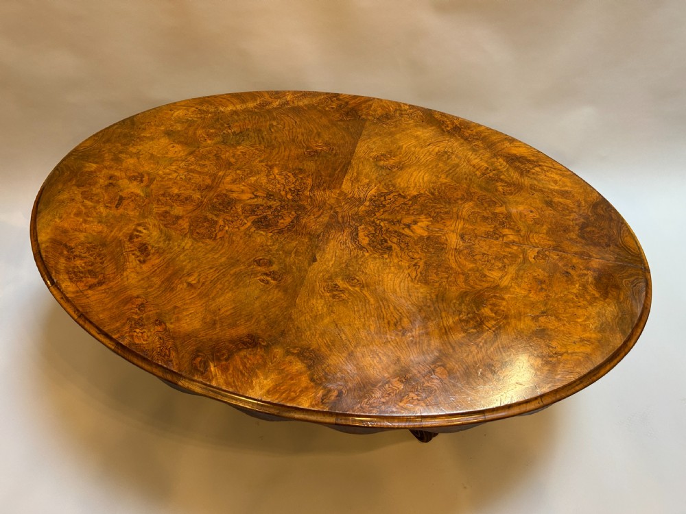 An oval Victorian burr walnut coffee table featuring a scalloped apron, figured wood grain top, and carved legs. View II