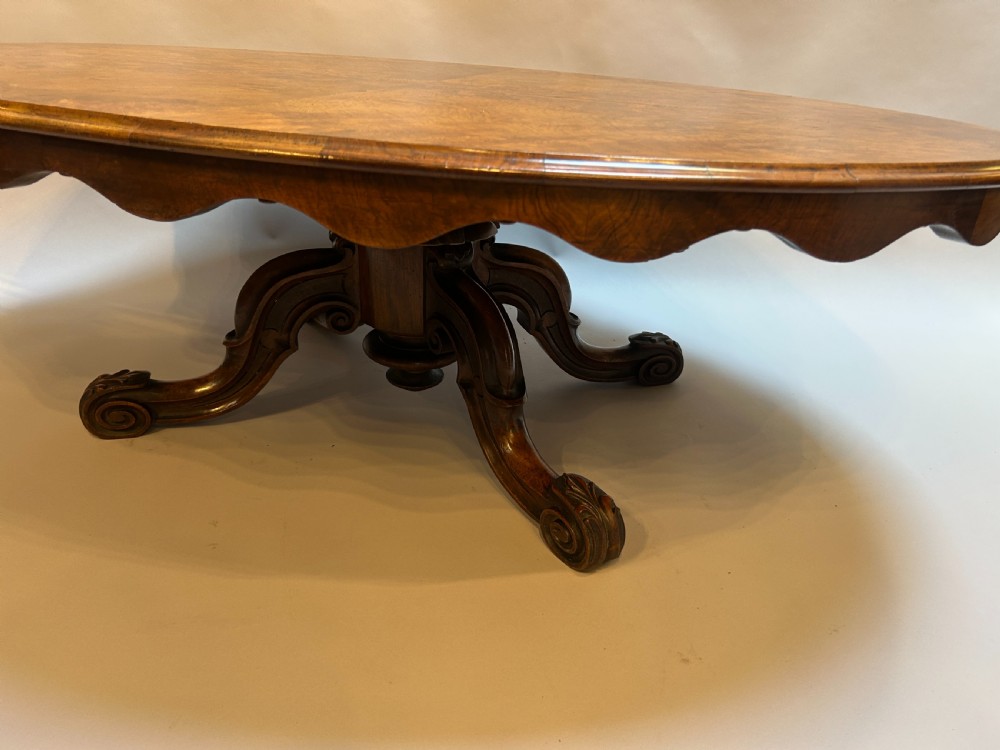 An oval Victorian burr walnut coffee table featuring a scalloped apron, figured wood grain top, and carved legs. View III