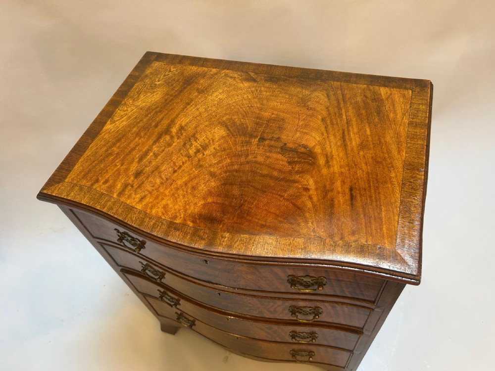 A small Georgian Revival chest of drawers featuring figured walnut veneer, four graduated drawers with brass handles, a serpentine front, and bracket feet. View II