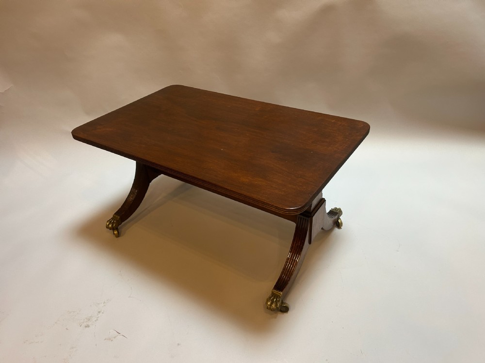 A rectangular George IV mahogany coffee table featuring reeded sweeping legs with brass lion paw castors.